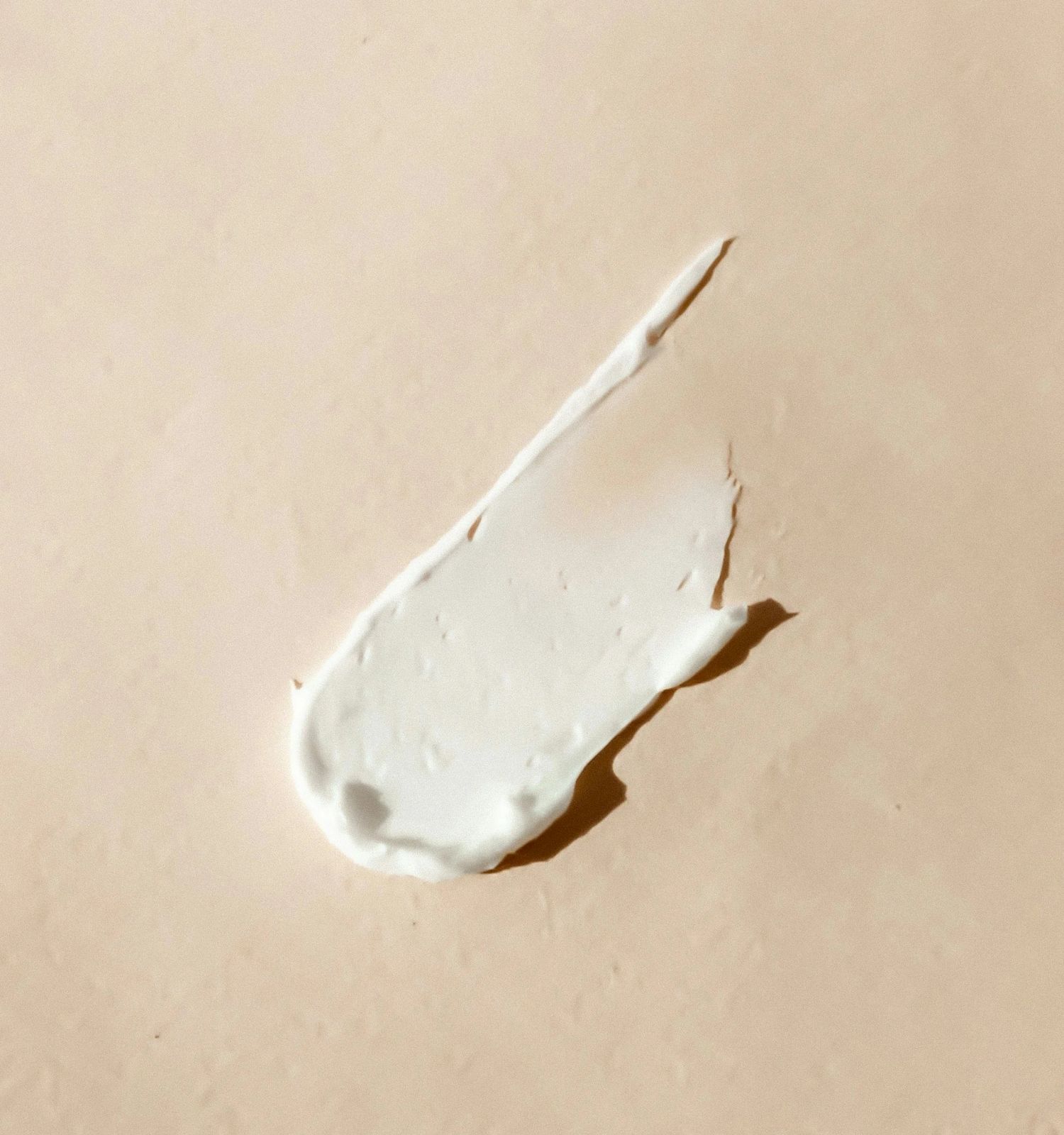 A smear of white cream or sunscreen on a beige surface, with a curved, tapering tip.